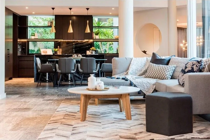 Modern living room and kitchen interior design with gray sofa, round coffee table, and stylish pendant lights over the kitchen island.