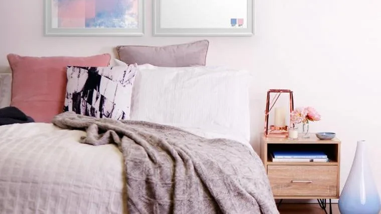 Cozy bedroom interior featuring a bed with pillows, a throw blanket, and a nightstand with floral decor. Home decor concept.